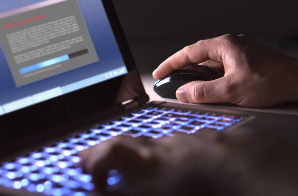 człowiek instalujący oprogramowanie w laptopie w ciemności w nocy. haker ładuje nielegalny program lub facet pobiera pliki. - tail fin zdjęcia i obrazy z banku zdjęć