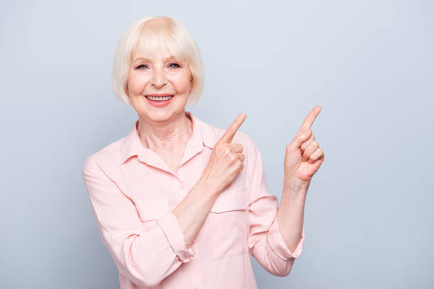 istock Old blonde glad lady smiling fingers pointing up over grey background, copy space 1033776828