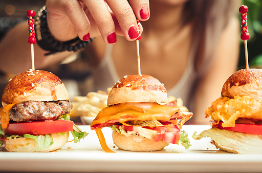 Woman eating mini burgers with fast food with French fries chips