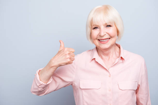 istock Old lady showing thumbs up gesture, smiling on grey background 1033777062