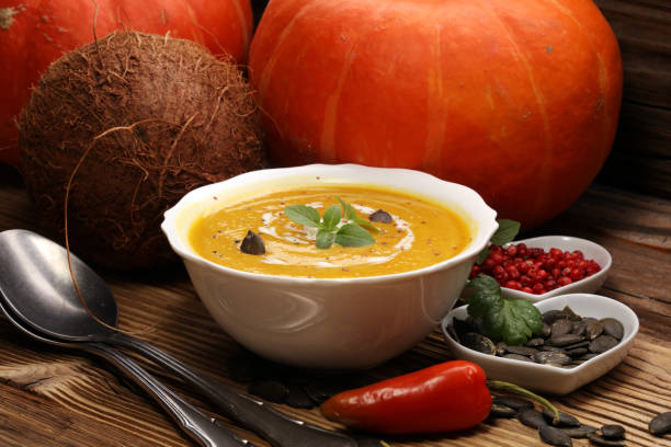 Roasted pumpkin and carrot soup with cream and pumpkin seeds on wooden background.
