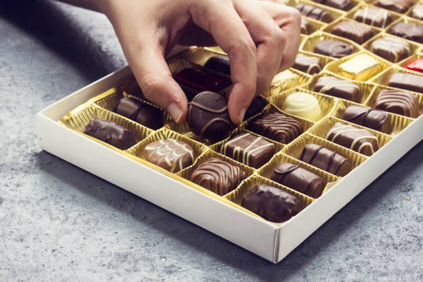 donna mano tenendo un pezzo di cioccolato di vario tipo in scatola per san valentino - pralina di cioccolato foto e immagini stock