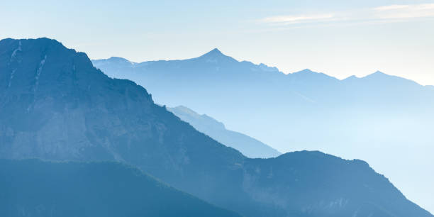 Photo of Distant blue toned mountain range of the majestic European Alps with mist and fog in the valley below
