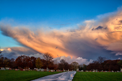 Late autumn extreme weather hailstorm under a vast, majestic but ominous, dusky purple and orange, spooky sunset cloudscape. Photo taken in November above a normally quiet and tranquil rural cemetery in western New York State near Rochester, NY.