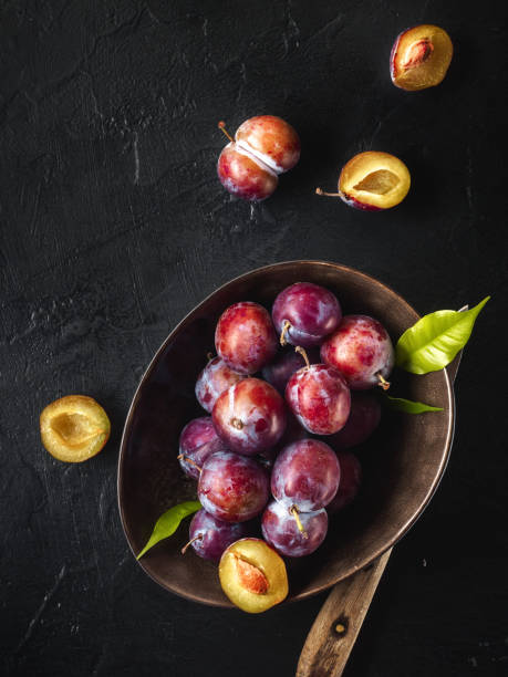 istock Whole fresh red violet blue plums and slices cut with knife in bowl on kitchen table 1033898678