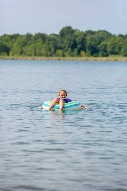 menina flutuando no tubo interno no lago, num dia de verão - inner tube swimming lake water - fotografias e filmes do acervo