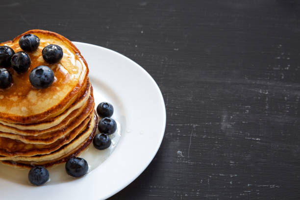 istock Pancakes with blueberries and honey over black background, side view. Copy space. 1033927506
