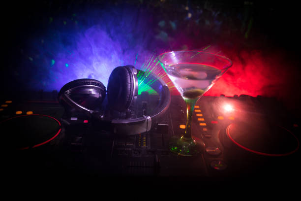 istock Glass with martini with olive inside on dj controller in night club. Dj Console with club drink at music party in nightclub with disco lights. Close up view 1033930964