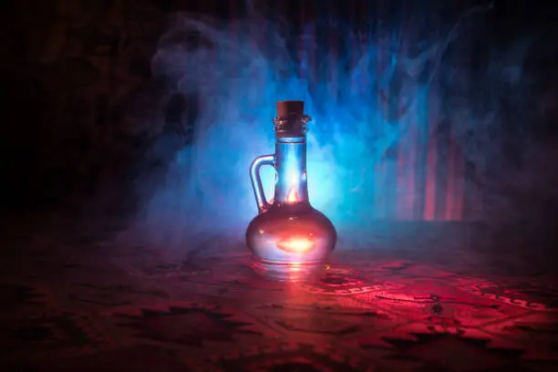 Photo of Antique and vintage glass bottles on dark foggy background with light. Poison or magic liquid concept.