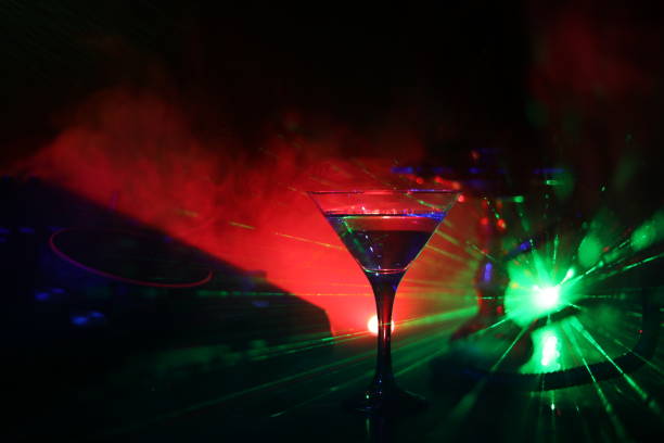 istock Glass with martini with olive inside on dj controller in night club. Dj Console with club drink at music party in nightclub with disco lights. 1033931086