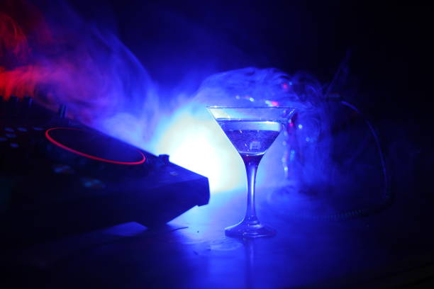 istock Glass with martini with olive inside on dj controller in night club. Dj Console with club drink at music party in nightclub with disco lights. 1033931096