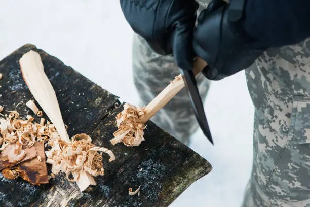 Man prepares wood-wool with hunting knife for starting fire. Wood shaving. Survival concept