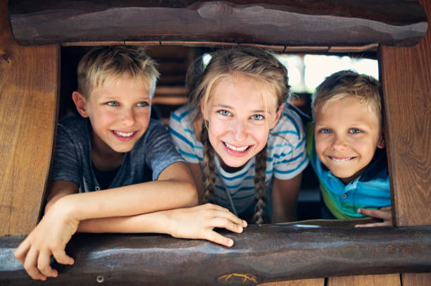 Three happy kids looking out of a tree house window