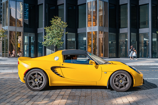 Man drives a yellow colored Lotus Elise sports car on Front street in Toronto, Ontario, Canada on a sunny day.