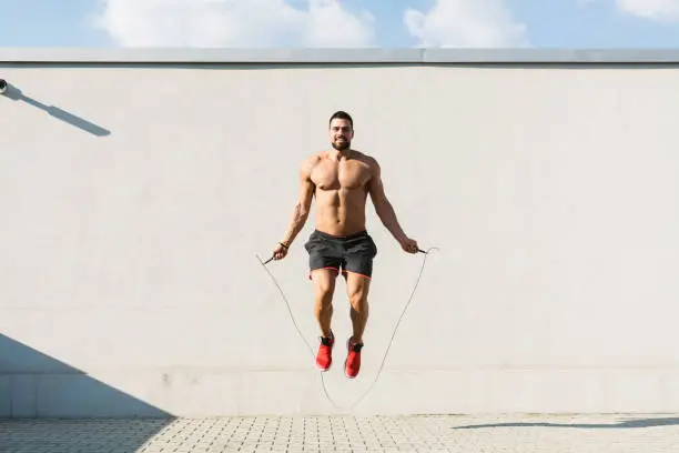 Young muscular man skipping rope outdoors front view
