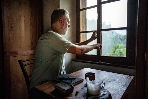 Mature Man Closing a Window on a Rainy Day.