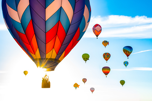 Balloons burning fuel as they fly over the city of Goreme in Cappadocia, with sightseeing tourists during a sunny summer day