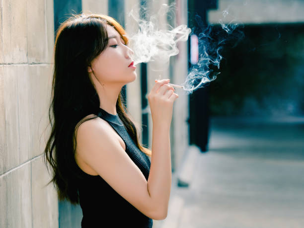 Portrait of beautiful Chinese girl smoking outdoor and thinking about problems, seems a little bit lost, in vintage mode. stock photo