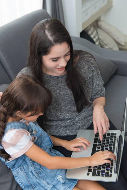 istock Beautiful young mom and daughter are using notebook on sofa at home 1034036514
