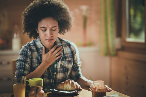African American woman feeling nausea during breakfast at dining table.