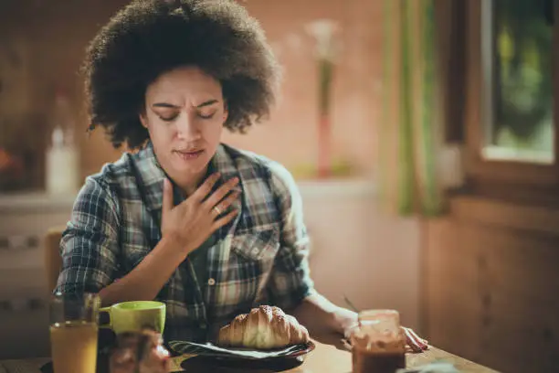 African American woman feeling nausea during breakfast at dining table.