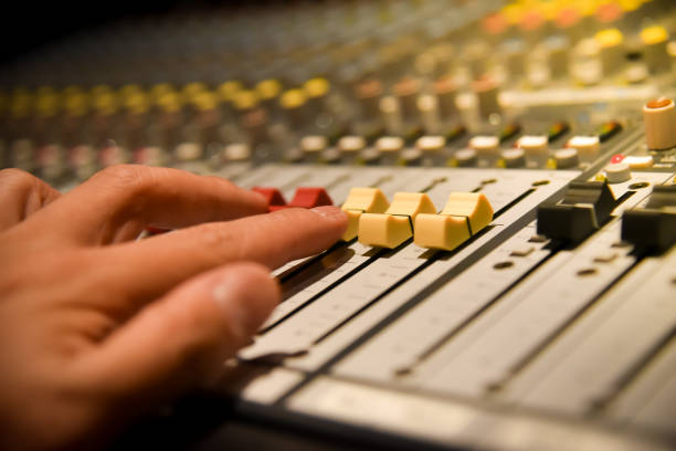 istock close-up hands of sound engineer adjusting audio mixer controller for live music and studio equipment. This is a quality audio system for professionals. vintage tone & effect light in control room. 1034135138