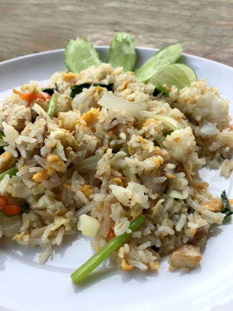 istock Asian fried rice with mackerel; egg and vegetable in white dish serve with slide cucumber on wooden background. Thai style food. 1034135322