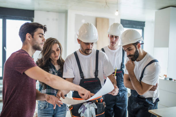 istock Young couple analyzing blueprints with team of manual workers. 1034138076