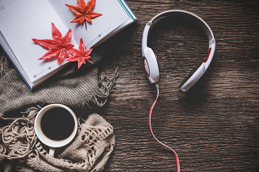 Cozy winter background, cup of hot coffee with marshmallow and headphone music and book note, warm knitted sweater, vintage tone. Lifestyle and music concept