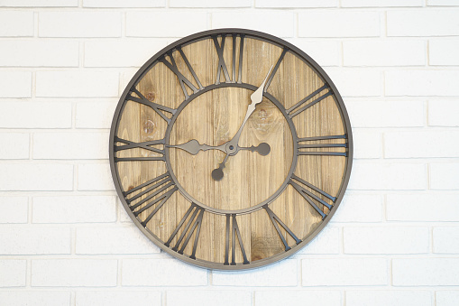 Wooden clock placed in middle of white brick wall