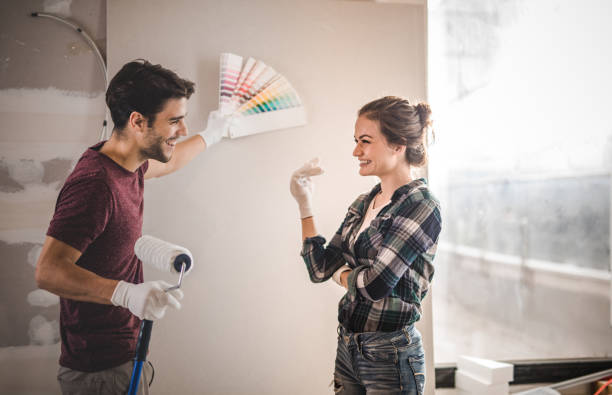 Happy couple choosing the right color for their wall while renovating apartment. Young couple talking while choosing the right color for their wall in new apartment. design color swatch painting plan stock pictures, royalty-free photos & images