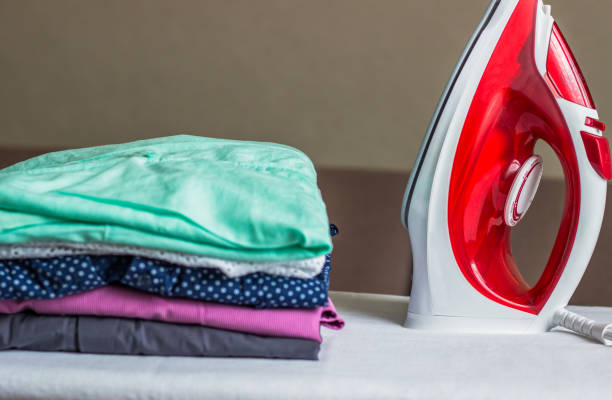 istock Iron on the ironing board and non-ironed clothes 1034162952