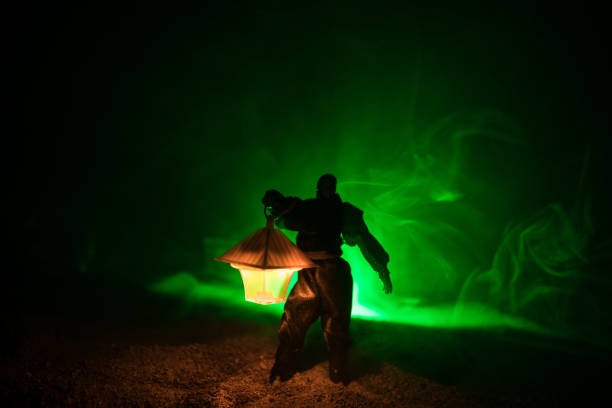 istock Man in raincoat coming from dark forest with glowing lantern in his hand concept. Silhouette of a horror killer with lamp 1034163070