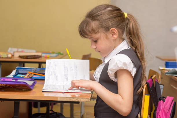 A little girl in a class carefully reads a diary entry A little girl in a class carefully reads a diary entry effective routine in children stock pictures, royalty-free photos & images