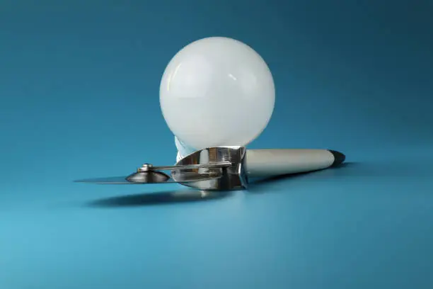 Photo of A perfectly white bulb with pizza knife lying on blue paper. Perfect design.