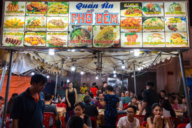Street restaurant at Ben Thanh Market area Ho Chi Minh City, Vietnam - April 28, 2018: open air night street restaurant at Ben Thanh Market. Signboard shows the menu with pictures & dishes names in Vietnamese and English. People sit at red tables. ho chi minh city photos stock pictures, royalty-free photos & images