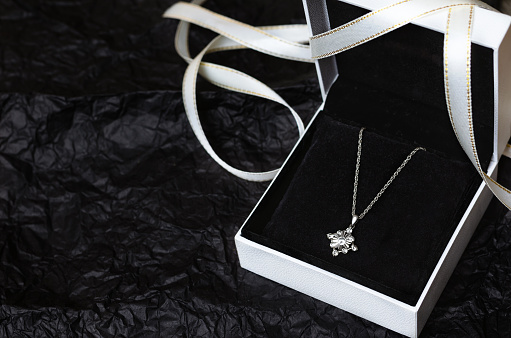 Silver necklace in white gift box on black background.