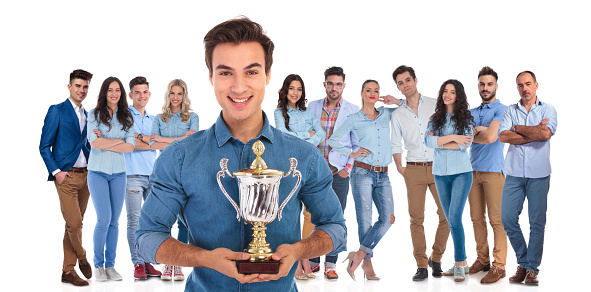 excited group leader of young casual team presenting you their winning cup while standing on white background in front of them