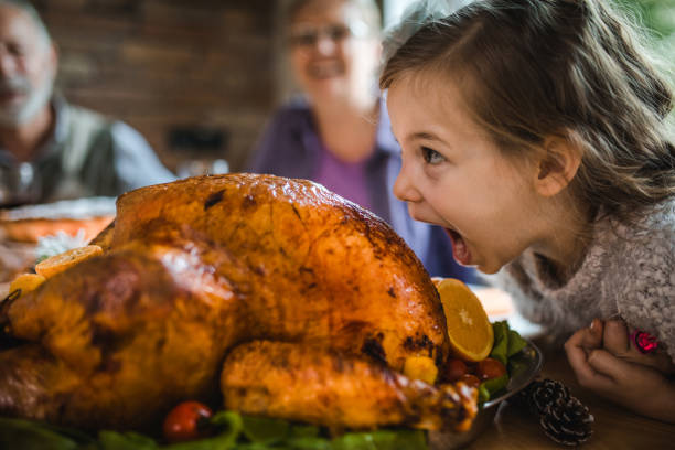 Small girl having fun while about to bite a roasted turkey on Thanksgiving. Cute little girl having fun while about to bite a stuffed turkey during Thanksgiving dinner in dining room. thanksgiving holiday photos stock pictures, royalty-free photos & images