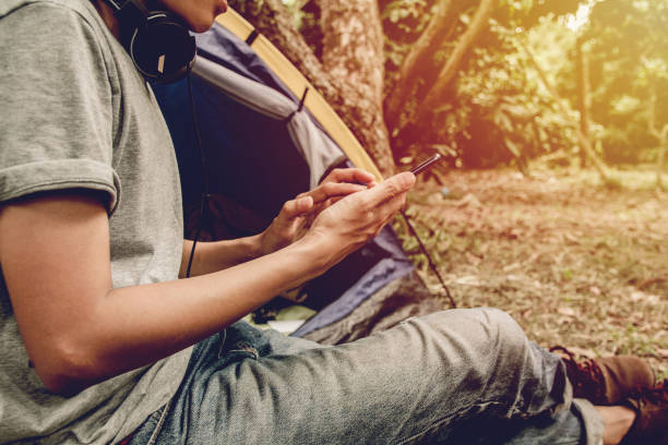 istock Asian young man sitting and using mobile phone in  outside the tent. Alone camping in forest. 1034227972