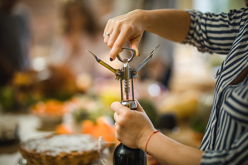 Close up of unrecognizable woman opening wine bottle with corkscrew.