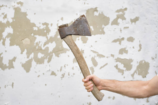 istock Old rusty ax in the man's hand against the shabby wall. 1034232442
