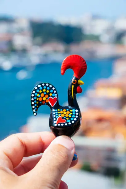 closeup of a young caucasian man with a traditional Rooster of Barcelos, the emblem of Portugal, in Porto, with the Douro river in the background