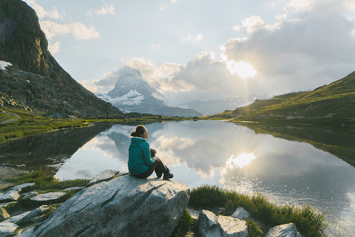 Young Caucasian woman sitting and  looking at scenic view of lake near Matterhorn mountain in Switzerland