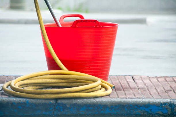 Equipment to wash car windshield, bucket and hose on sidewalk. Copy space available on the right.