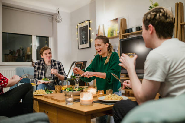 Young Couples Having Dinner at Home Two young couples are having a dinner party and one woman is laughing while serving salad. college dorm party stock pictures, royalty-free photos & images