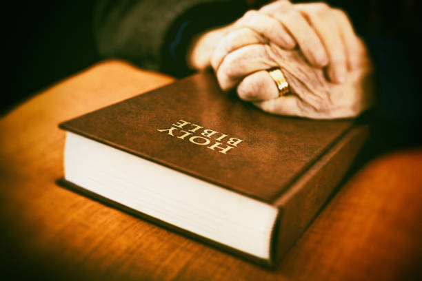 istock Senior woman's folded hands on closed Bible 1034252614