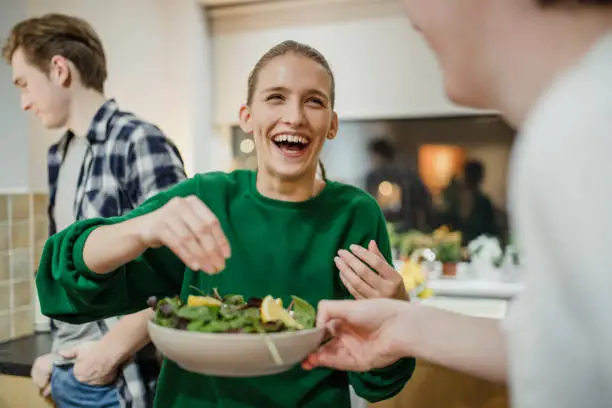 Young woman is laughing with her friends at a dinner party as she squeezes lemon juice on a salad.