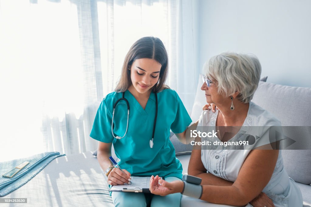 Enfermera mide presión de mujer mayor en casa - Foto de stock de Doctor libre de derechos