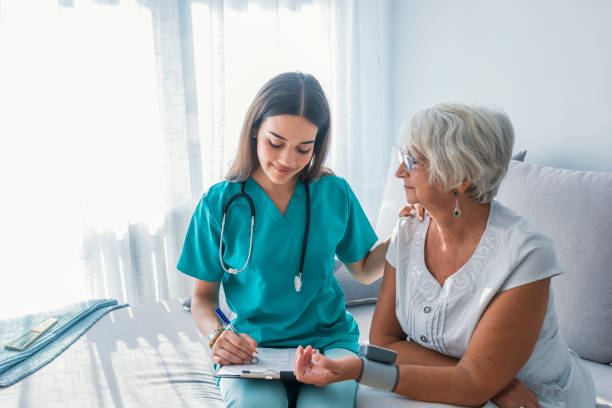 Nurse measuring blood pressure of senior woman at home Nurse doing blood pressure monitoring for senior woman at home. Close up photo of blood pressure measurement. Nurse measuring blood pressure of senior woman at home. Smiling to each other. assistant stock pictures, royalty-free photos & images